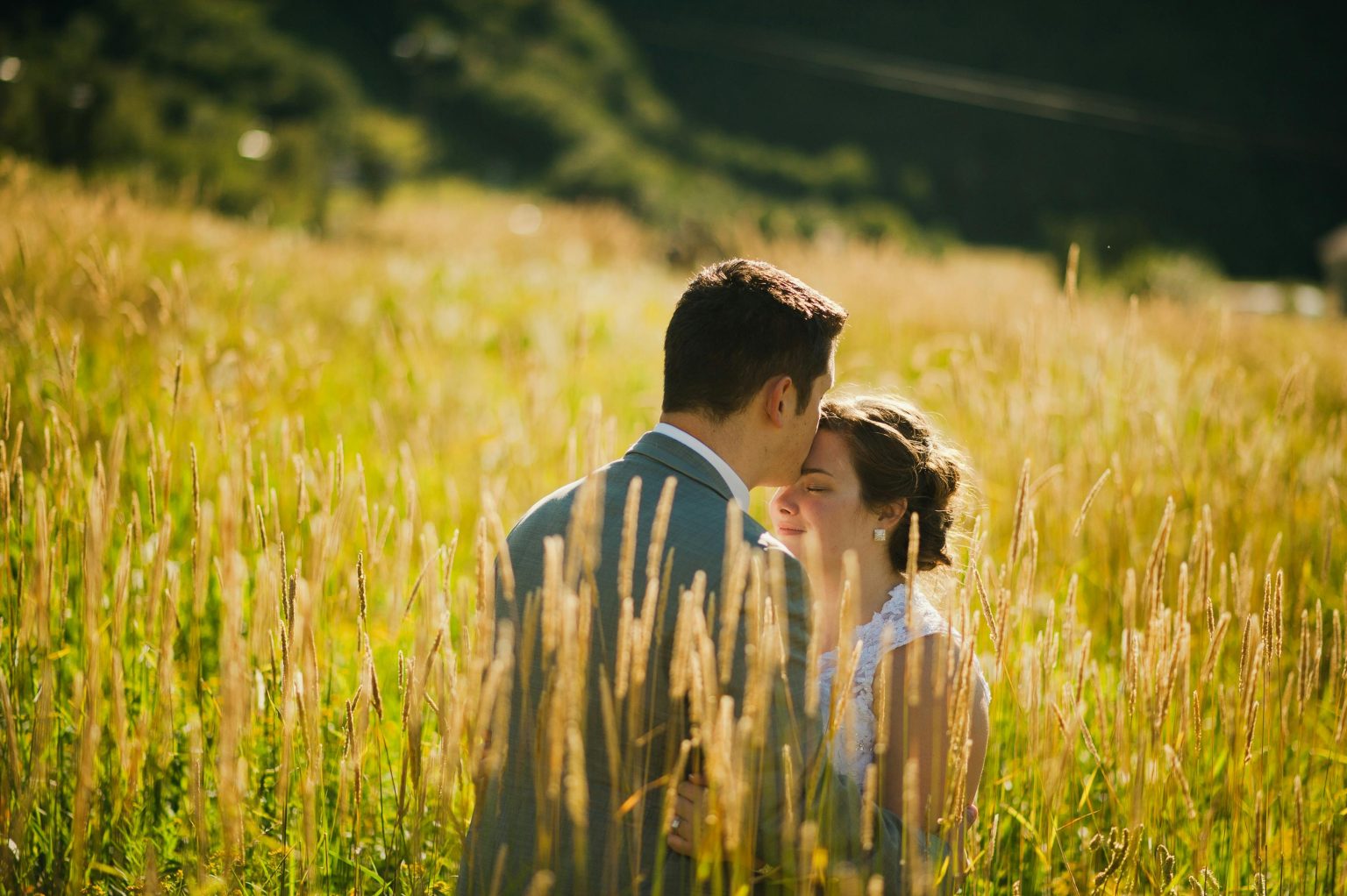A couple shares a tender moment in a sunlit wheat field, exuding warmth and romance.