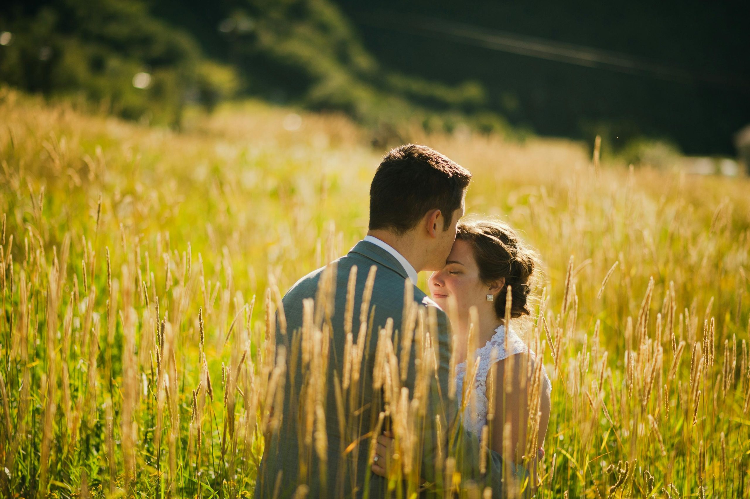 A couple shares a tender moment in a sunlit wheat field, exuding warmth and romance.
