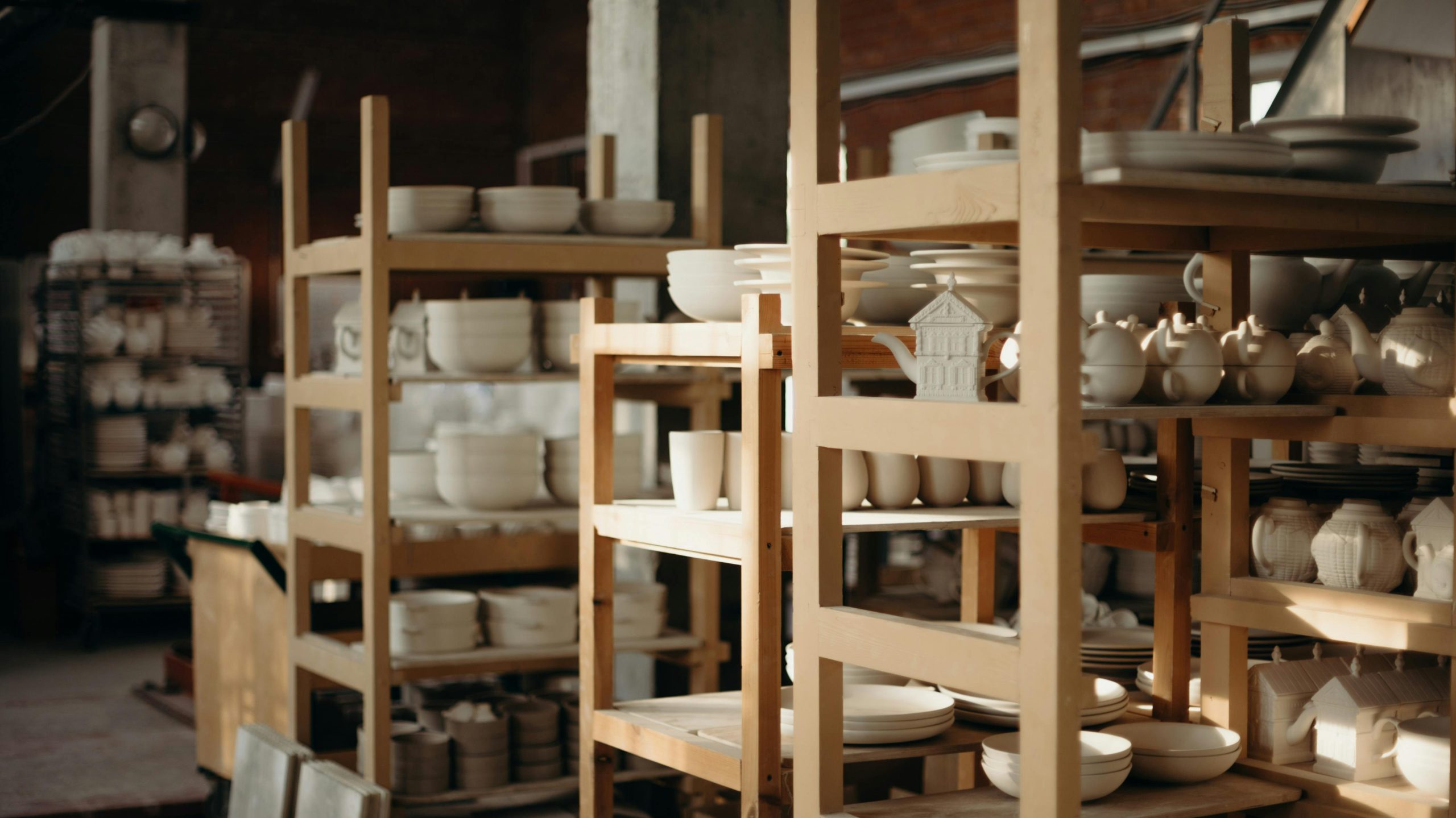Explore a rustic pottery workshop with handmade ceramics, showcasing bowls, mugs, and teapots on wooden shelves.