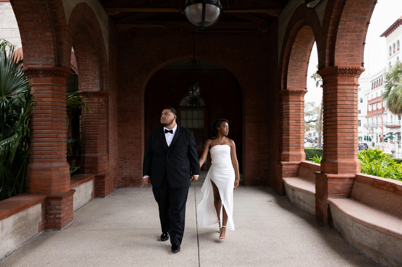 A couple in formal attire walking under beautiful red brick arches, capturing timeless elegance.